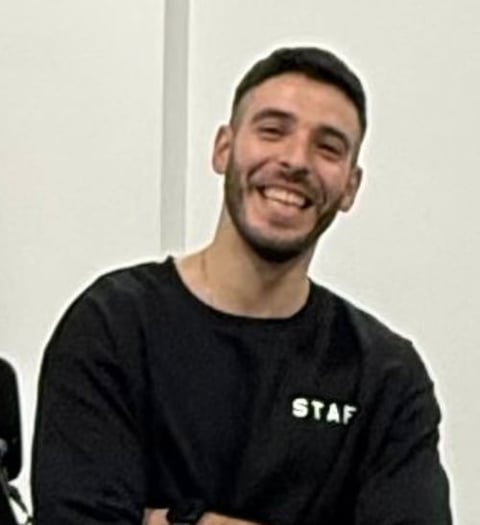 Man smiling at camera wearing black STAF t-shirt against white background