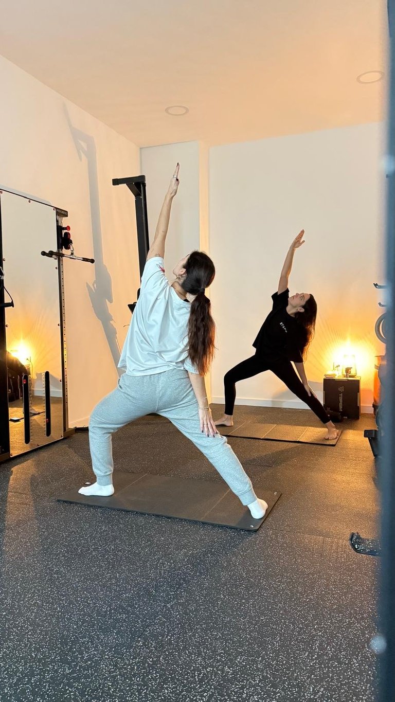 Two women performing yoga poses in a mirrored studio with warm lighting and potted plants
