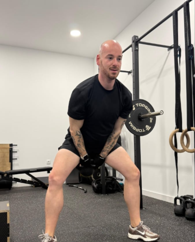 Man performing barbell exercise in gym with rig equipment and gymnastics rings visible in background